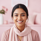 A happy young adult South Asian woman with a warm smile, looking at the camera. The background is softly blurred with rose an
